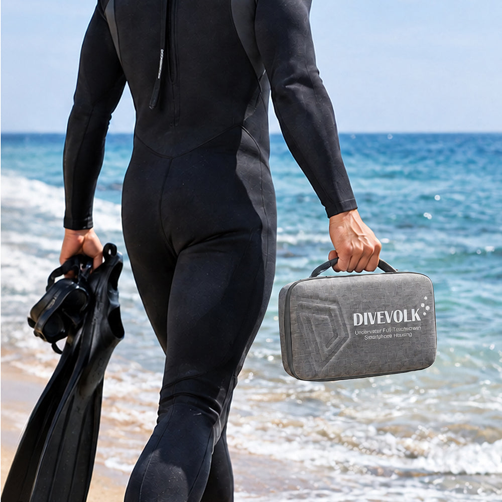 Diver in wetsuit walking into ocean ¡ª carrying DIVEVOLK grey travel case in one hand and dive fins in the other, beach dive trip ready.